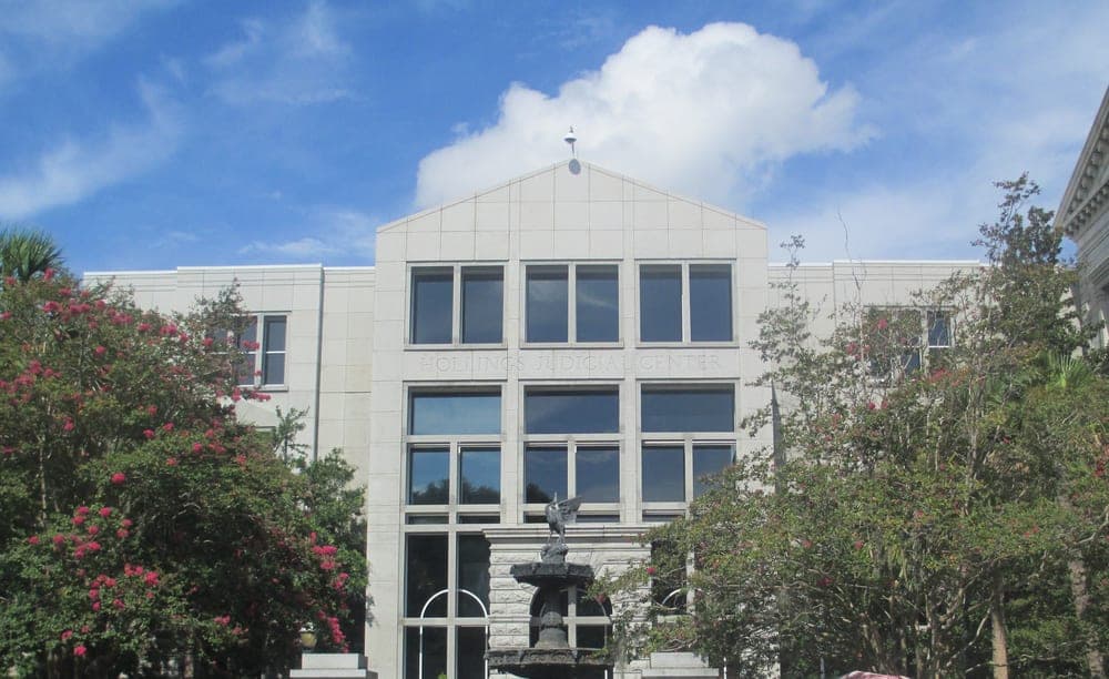 Exterior of the J. Waties Waring Judicial Center, the federal courthouse in Charleston, South Carolina, a modern limestone building with tall windows and a fountain in its forecourt, its facade engraved 'Hollings Judicial Center'