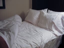 A made bed with white linens, two pillows, and a dark headboard — a representative file photo of a mattress and bedroom, not a specific Avenco or Novilla model