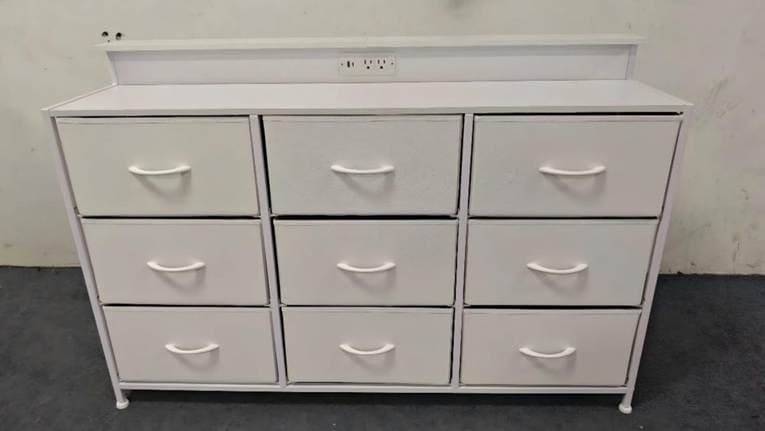 A white DUMOS nine-drawer fabric dresser: nine soft-sided fabric drawers in a three-by-three grid on a metal frame, with a raised back panel holding built-in power outlets.