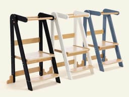 Three HARPPA Nordi foldable toddler tower stools in black, white, and blue finishes with natural-wood steps, platforms, and safety bars, standing side by side against a plain background.