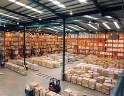 Interior of a modern warehouse showing tall metal pallet racking filled with palletized goods and a forklift in the aisle, with no people in frame.