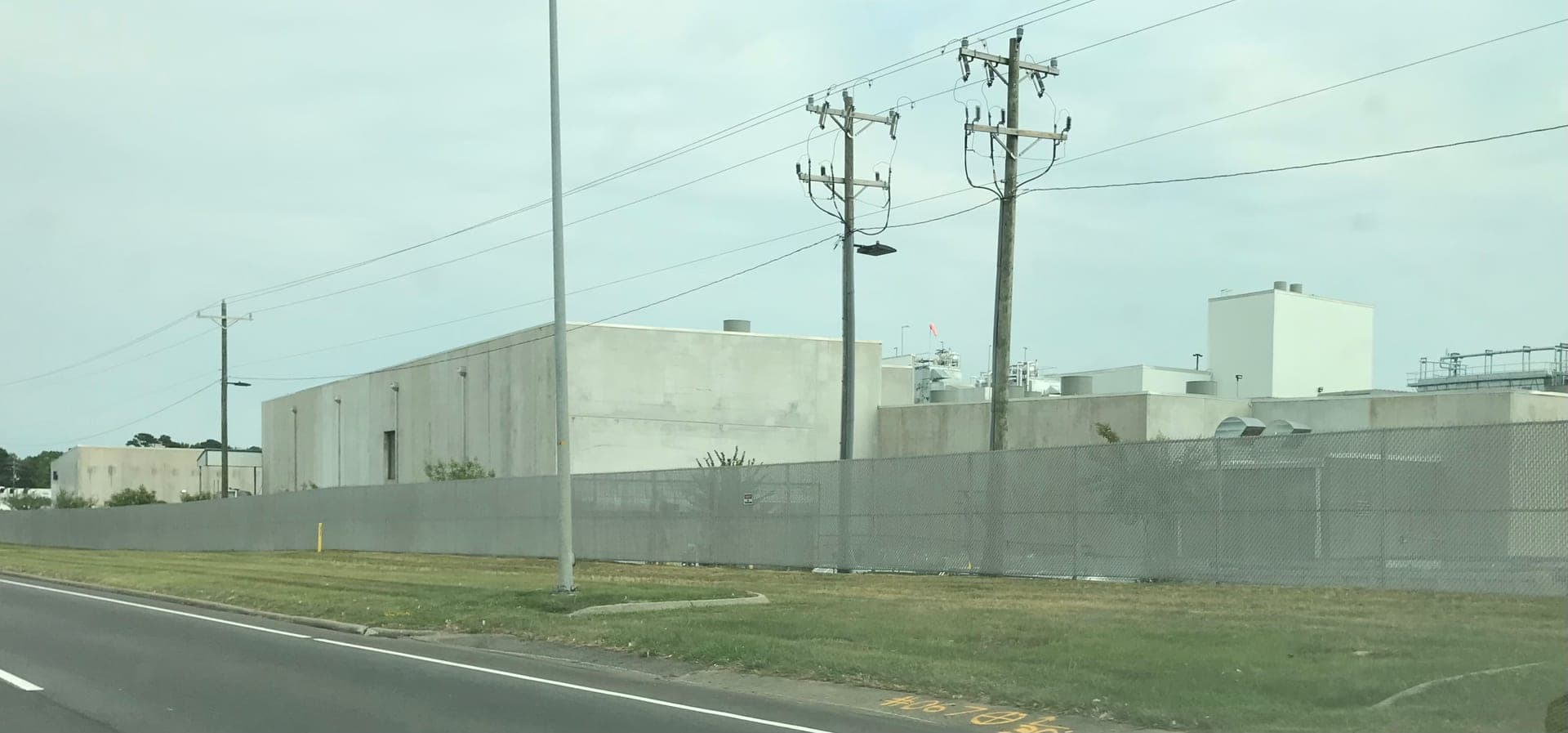 Exterior of a large modern poultry processing plant behind a perimeter fence on an overcast day, with windowless concrete process buildings and rooftop equipment.