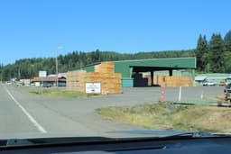 A wood-products mill in the Pacific Northwest, with stacks of finished lumber in the yard and a forested hillside behind.
