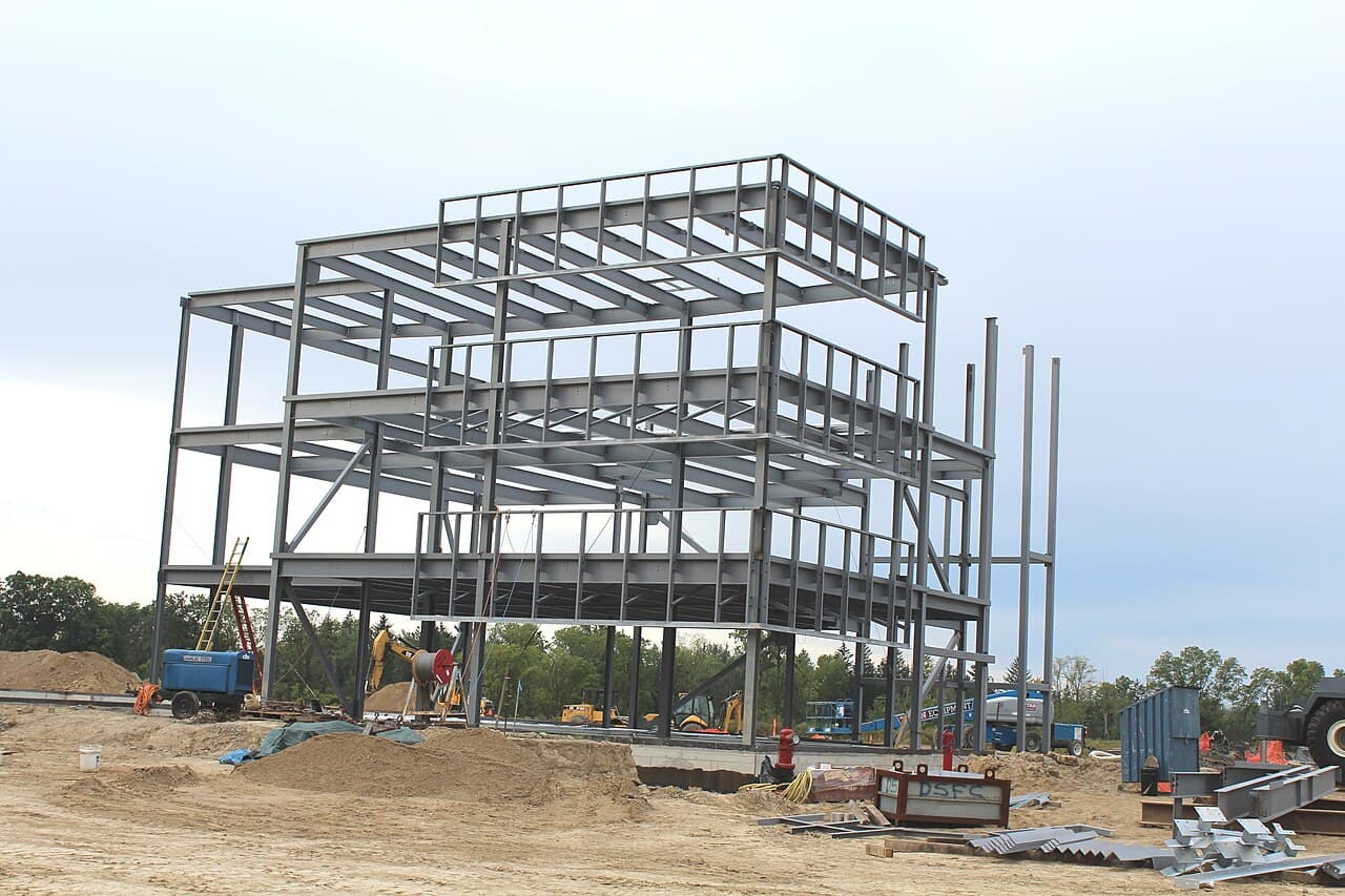 A multi-story steel-frame commercial building under construction at a job site, showing open structural floors and unguarded edges at height.
