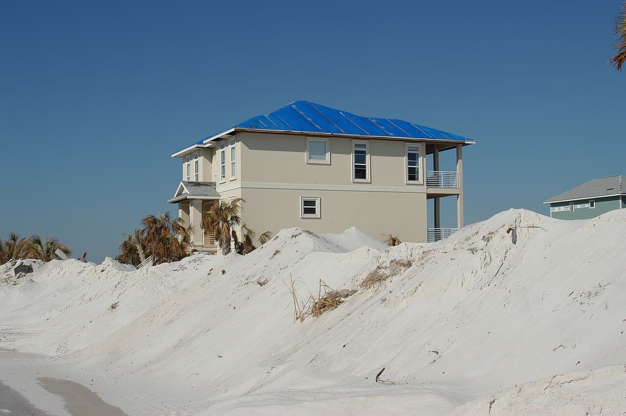 A Florida house with a full blue emergency tarp installed over its damaged roof under a clear sky.
