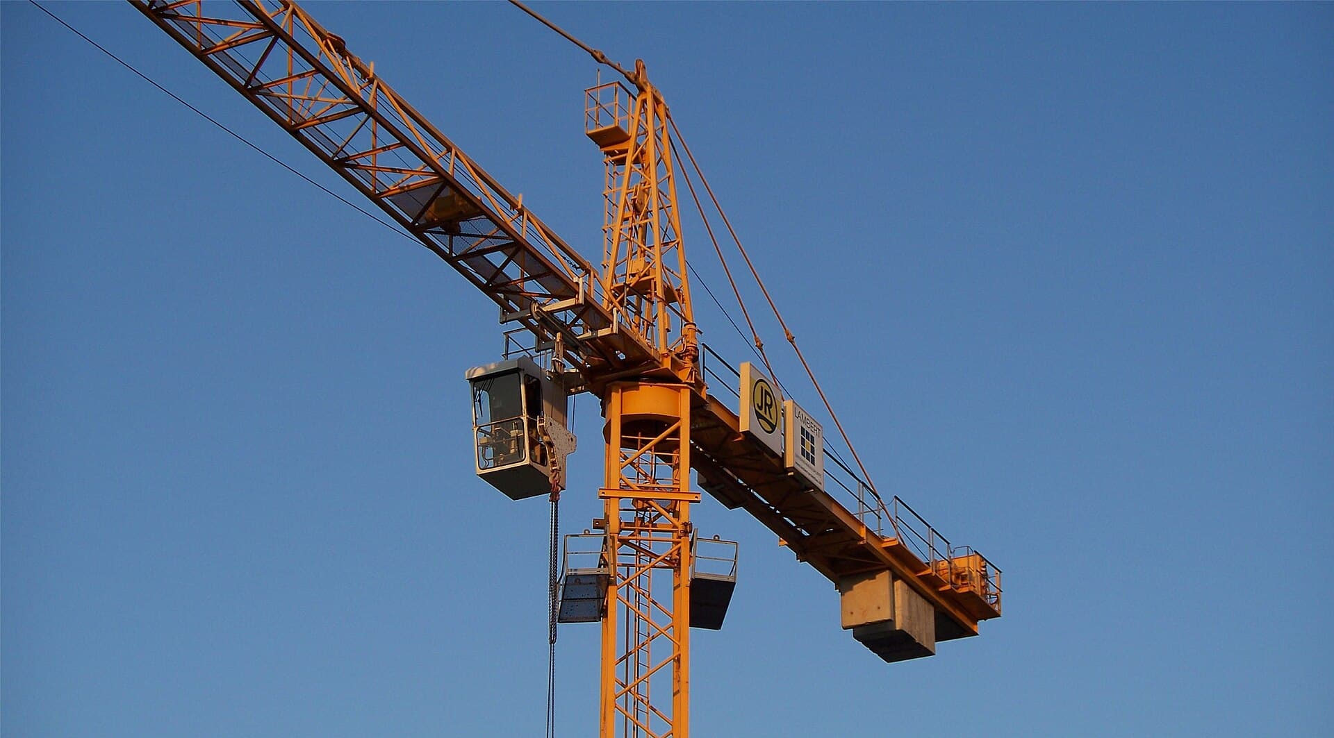 The jib and operator cab of a construction tower crane silhouetted against a clear blue sky.