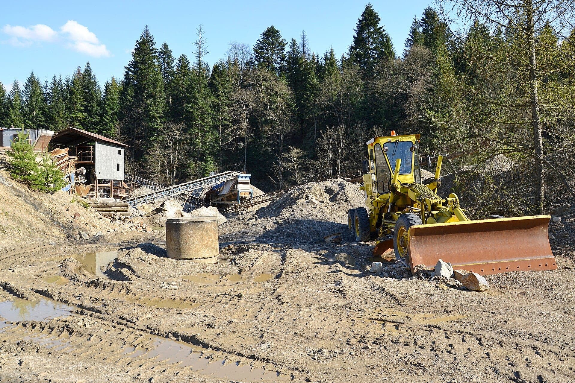 A rock crusher with a feed conveyor and a wheel loader at an outdoor aggregate processing site.