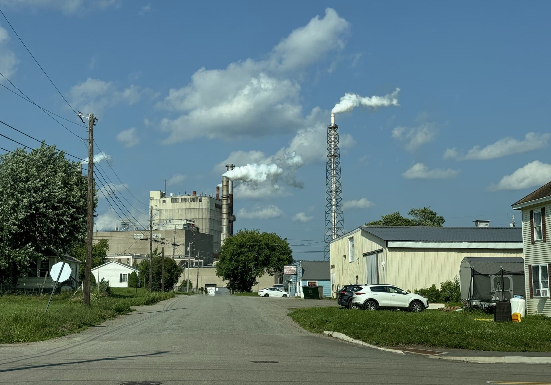 The Woodland Pulp mill in Baileyville, Maine, with steam rising from two stacks, seen from a nearby residential street.