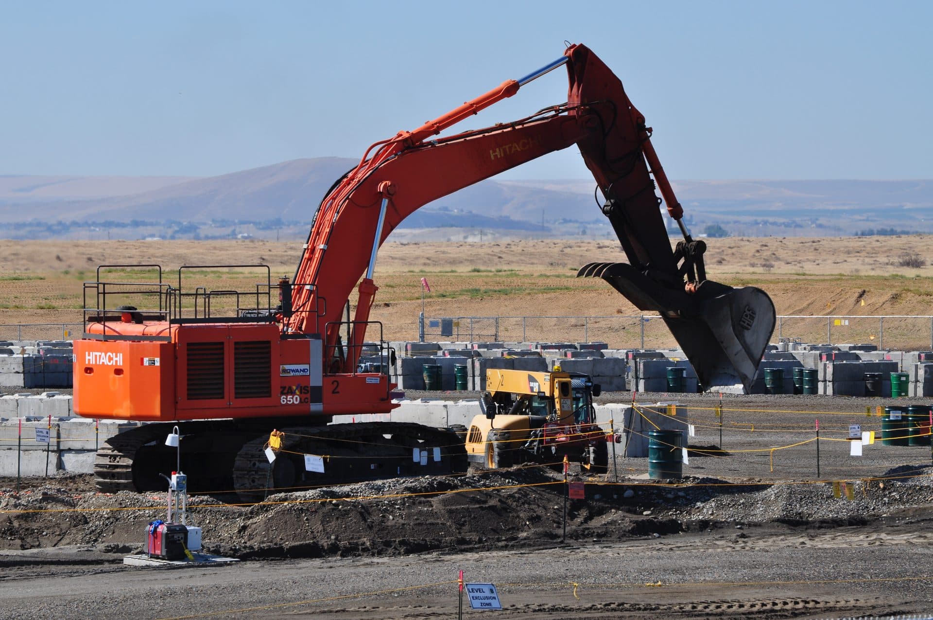 An excavator machine digging into an open trench at the Hanford 618-10 Burial Ground remediation site — no workers are visible inside the trench